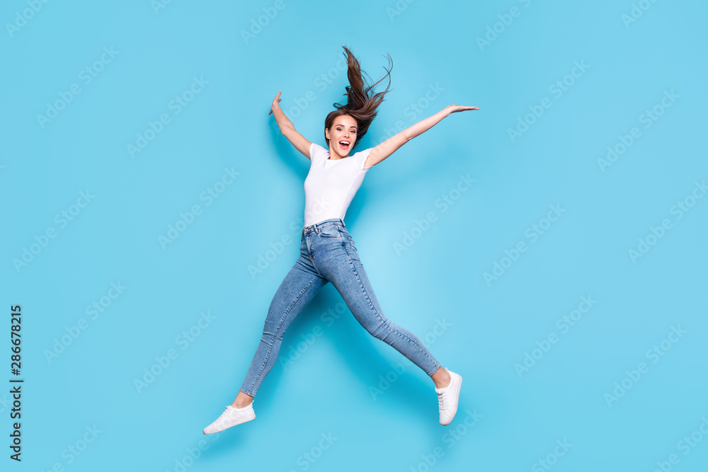 Full size photo of pretty teen raising hands screaming laughing wearing white t-shirt denim jeans sneakers isolated over blue background