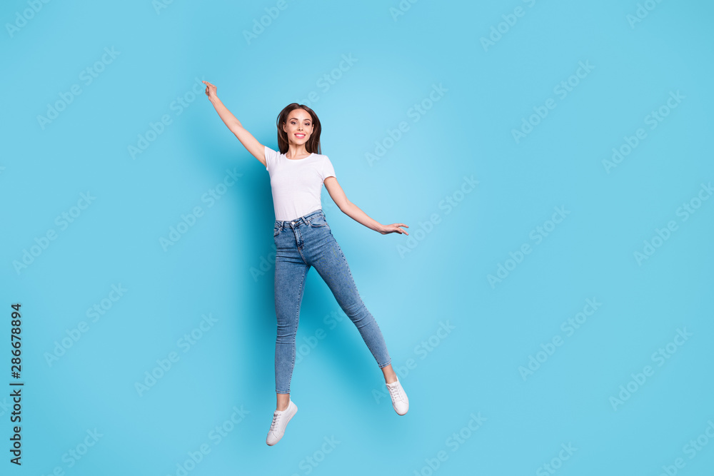 Full body photo of cute youngster raising arms up wearing white t-shirt denim jeans sneakers isolated over blue background