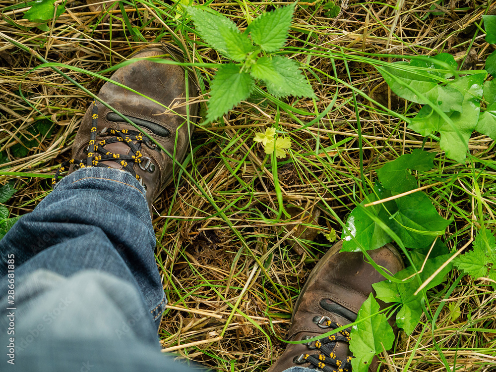 Old worn boots on forest ground between leafs and grass and blue jeans. Close up. Concept: traveler, tourist, adventure, experience. Old worn boots on forest ground between leafs and grass and blue jeans. Close up. Concept: traveler, tourist, adventure, experience.