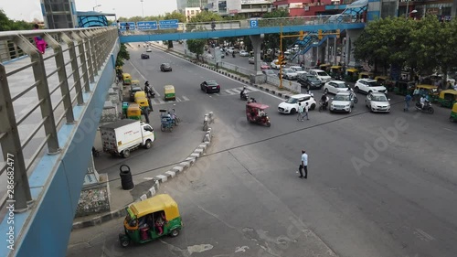 Time-lapse top view looking down at busy road intersection with vehicular traffic movement next to a modern CBD and commercial hub with a metro line  in national capital of Delhi, India photo