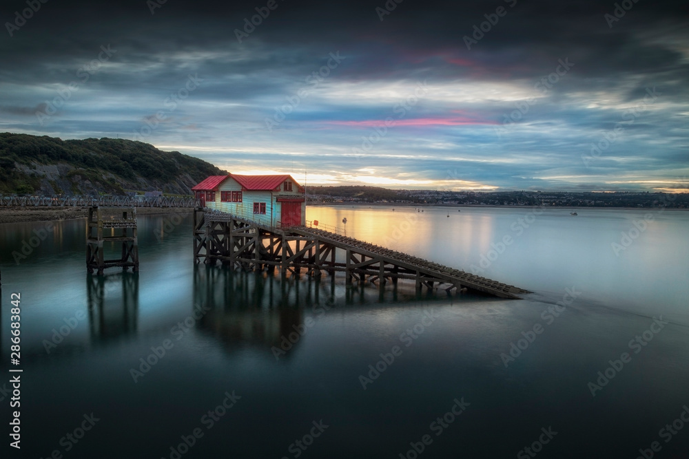 Sunset and a calm evening tide at the old lifeboat station on Mumbles Pier, Swansea Bay, South Wales, UK Sunset and a calm evening tide at the old lifeboat station on Mumbles Pier, Swansea Bay, South Wales, UK
