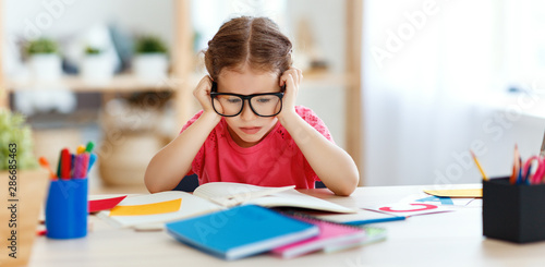 tired child girl doing her homework at home.