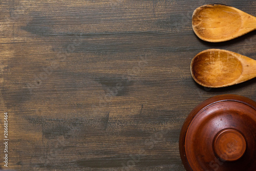 Top view of clay pot and wooden spoons on wooden background with copy space