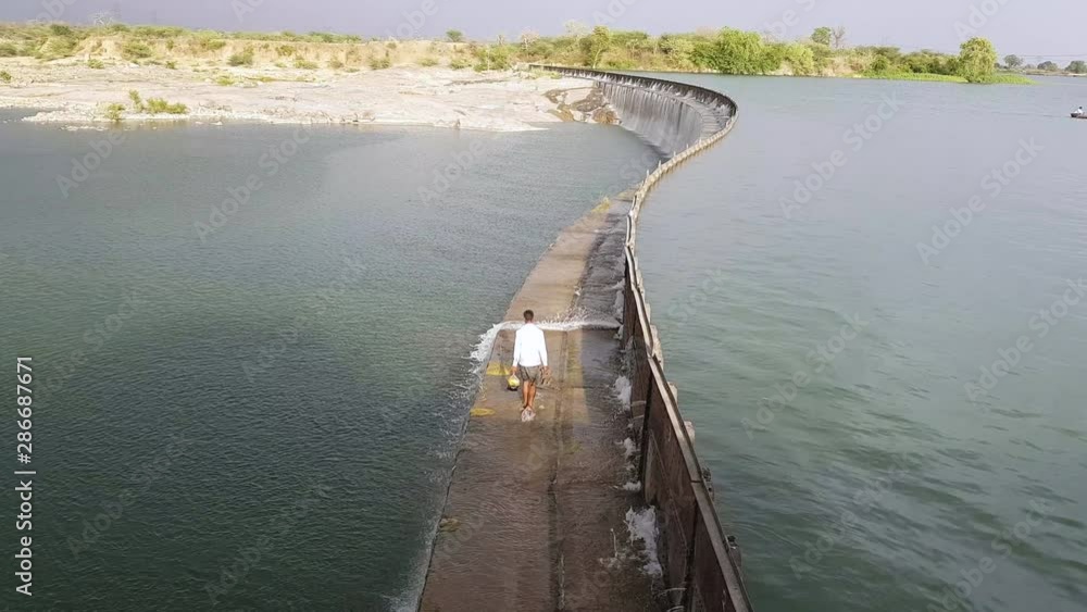 Wide, man carrying bags crossing the Parichha Dam on the Betwa River in India Wide, man carrying bags crossing the Parichha Dam on the Betwa River in India