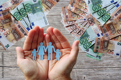 Paper family in hands on wooden background with euro banknotes 