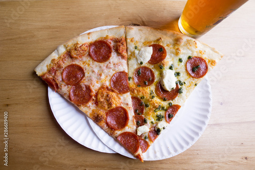 two slices of pizza with mozzarella pepperoni ricotta and pesto on white plates with a beer cropped
