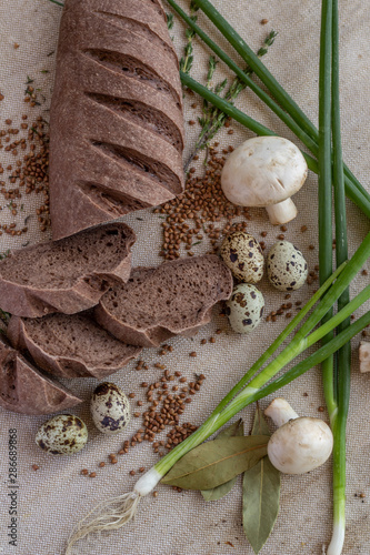 composition of dark sliced ​​bread with scattered buckwheat, sprigs of rosemary, fresh mushrooms, quail eggs and green onions on baking canvas