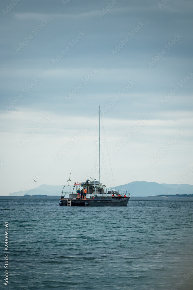 Moody sea view with yacht, clouds and hills