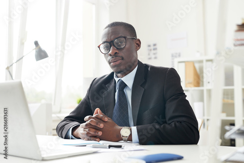 Portrait of African entrepreneur sitting at his workplace at office and looking seriously and confidently