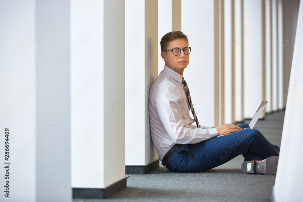 Young businessman using laptop while sitting on floor at office Young businessman using laptop while sitting on floor at office