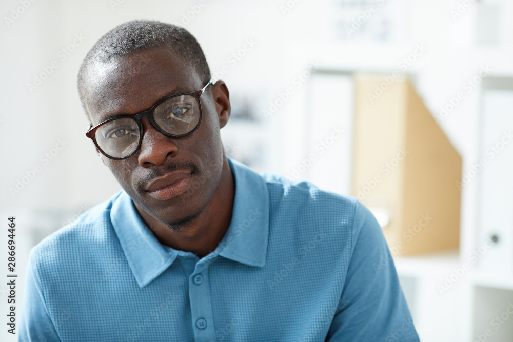Portrait of young handsome African man in eyeglasses and in blue shirt looking at camera Portrait of young handsome African man in eyeglasses and in blue shirt looking at camera