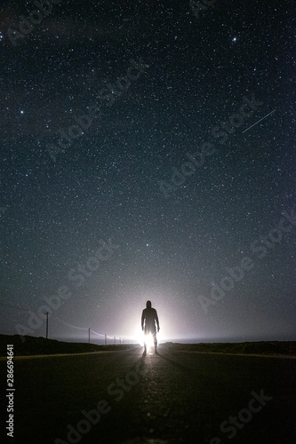 Silhouette of a man at night, under the stars lit by a lighthouse in Sagres, Portugal