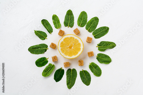 Composition of mint leaves, lemon and pieces of cane sugar on a white old concrete background.