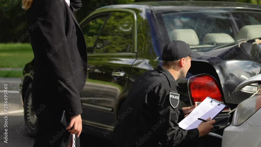 Policeman examining car accident and making notes, nervous woman walking around Policeman examining car accident and making notes, nervous woman walking around