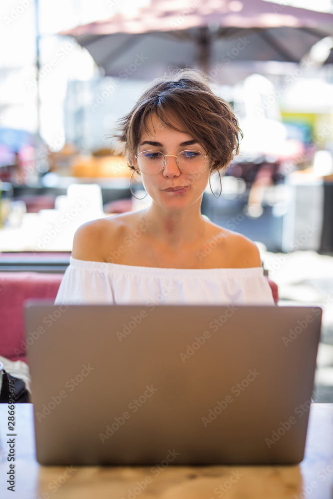 Attractive female freelancer sitting at wooden table front open computer in modern coffee shop Attractive female freelancer sitting at wooden table front open computer in modern coffee shop