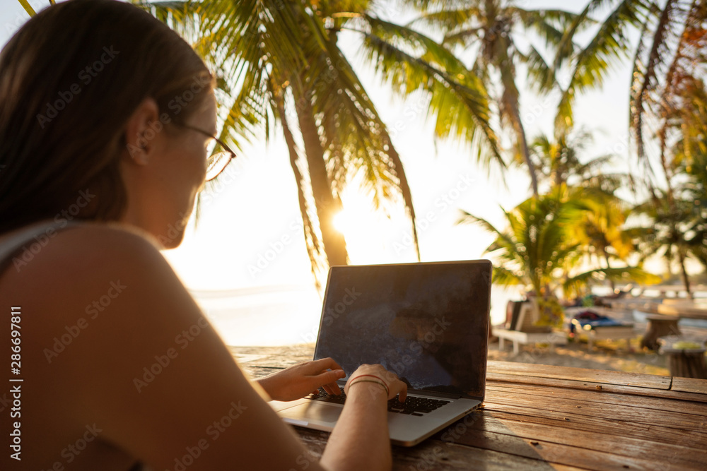 freelancer girl with a computer among tropical palm trees work on the island in sunset