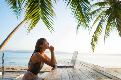 freelancer girl with a computer among tropical palm trees work on the island in sunset photo