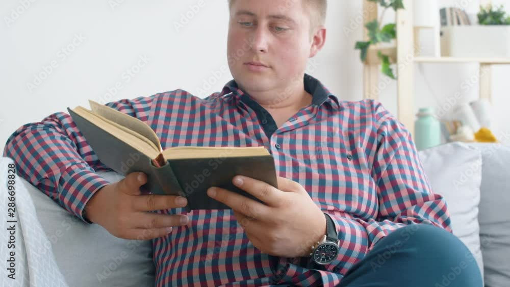 Man seat on sofa in living room and read interesting book. Relaxing after work. 4k. Slow motion. Man seat on sofa in living room and read interesting book. Relaxing after work. 4k. Slow motion.