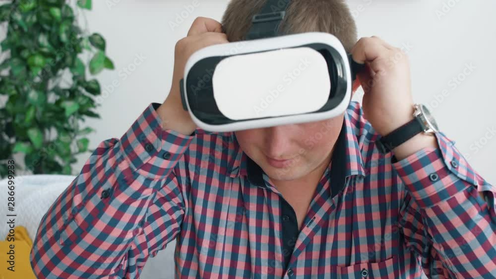 Young guy playing games in virtual reality glasses when seat on sofa in living room. Vr games playing in home. 4k slow motion footage. Young guy playing games in virtual reality glasses when seat on sofa in living room. Vr games playing in home. 4k slow motion footage.