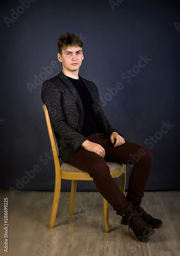 A young man of European appearance, in formal clothes is sitting on a chair. Shooting in the studio, plain gray background.