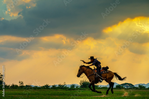 a cowboy rider is riding horseback in ray light sunset