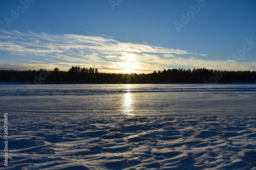 Frozen lake during sunset under a blue sky with trees' silhouette.