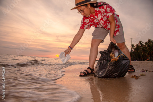 Asian women tourists picking up plastic garbage cleaning on the beach During the sunset . Tourists volunteers are helping to collect garbage picking up trash . Cleaning environmental pollution