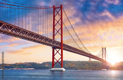 25th April Bridge in Lisbon  Portugal. Famous landmark on river Tagus. Summer sunny landscape with evening dusk sunset sky with clouds and sunlight.