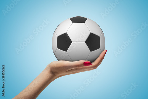 Side closeup of woman s hand facing up and holding new football on light blue background.
