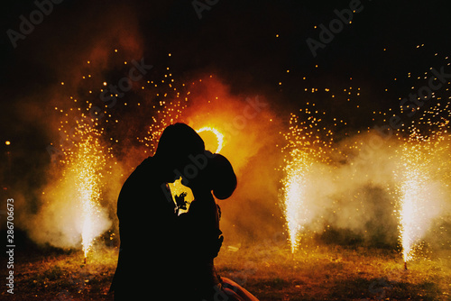 Silhouettes of the bride and groom on the background of fire shows and pyrotechnic lights