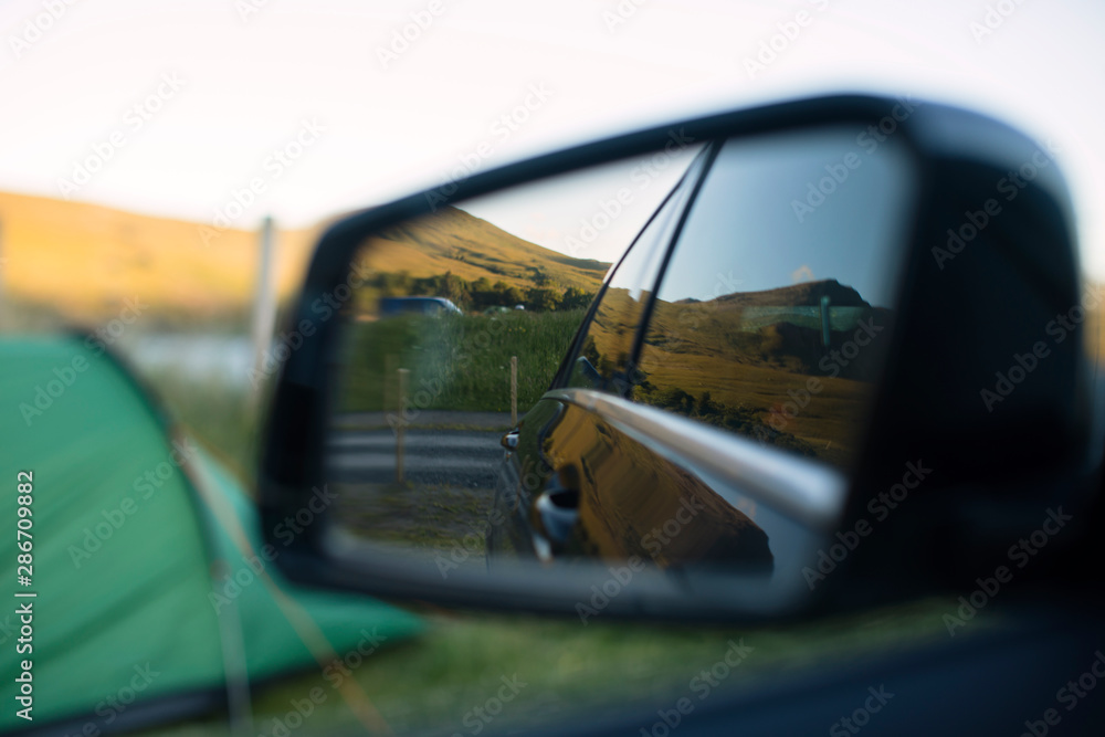 Scenic campsite with a green tent and mountains reflected in a parked car