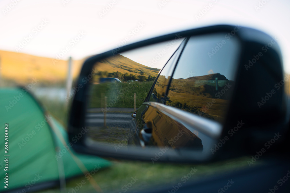 Scenic campsite with a green tent and mountains reflected in a parked car Scenic campsite with a green tent and mountains reflected in a parked car