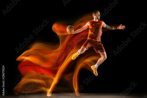 Becoming a winner. Young caucasian basketball player of red team in action and jump in mixed light over dark studio background. Concept of sport, movement, energy and dynamic, healthy lifestyle. © master1305