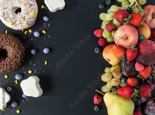 A lot of natural and healthy vitamin fruits, berries vs sweet and junk food on a black background. Vegan eco safe food. The right foods for weight loss and the wrong foods for weight gain. The choice