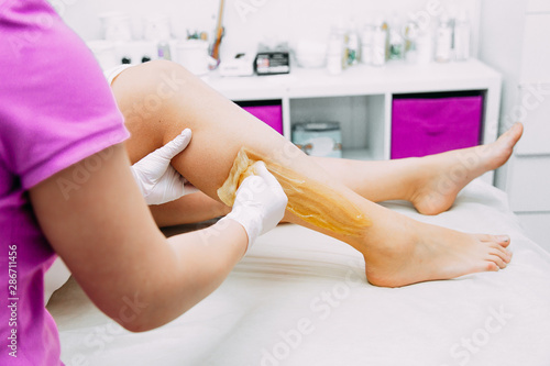 Young woman depilating legs with liquid sugar in spa center. Close up.