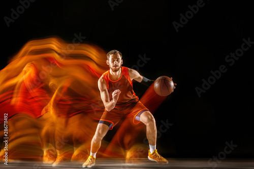 Becoming a winner. Young caucasian basketball player of red team in action and jump in mixed light over dark studio background. Concept of sport, movement, energy and dynamic, healthy lifestyle.