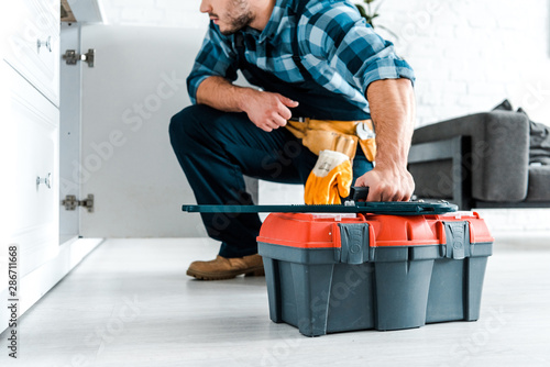 cropped view of bearded handyman sitting and holding toolbox photo