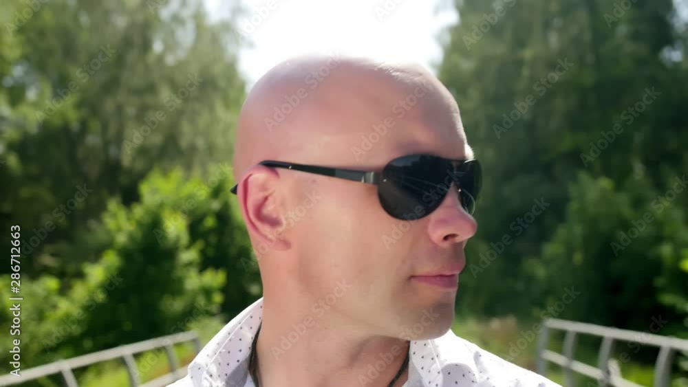 Portrait of a bald man with sunglasses against the background forest. Looking into the camera. Close up shot. Portrait of a bald man with sunglasses against the background forest. Looking into the camera. Close up shot.