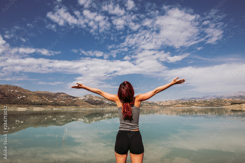 happy woman opens her arms in front of a lake on a trip with much happiness
