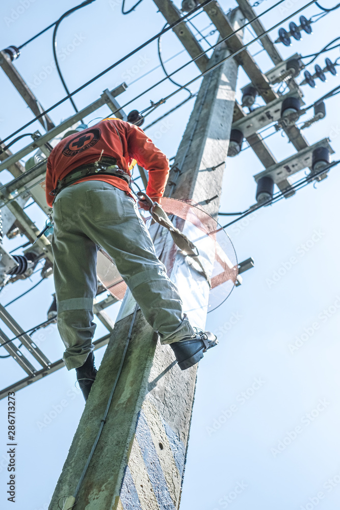 Electrician lineman with safety belt climb electric post power pole to install and repair power lines. Electrician lineman with safety belt climb electric post power pole to install and repair power lines.