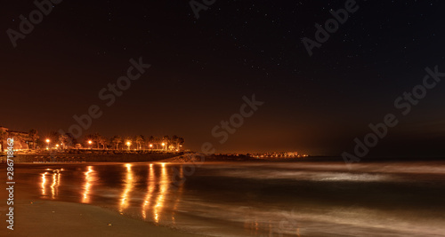 At night on the beach near Torrevieja in Spain. A long exposure with soft waves and beautiful lights of the lanterns on the promenade. Stars in the sky.