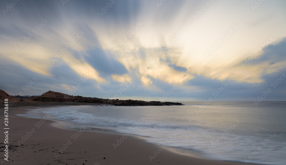 A beautiful bay with a sandy beach in the early morning before sunrise near the Spanish town of Torrevieja. Colorful clouds in the sky. Soft waves through long exposure.