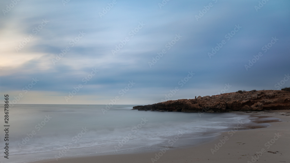 Half an hour before sunrise. A beautiful bay for swimming with a sandy beach in the early morning before sunrise near the Spanish town of Torrevieja. Soft waves through long exposure.