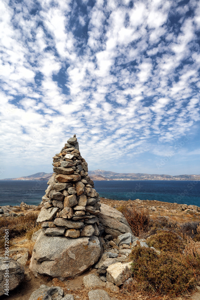 Cairn of rocks and cloudscape at Agios Prokopios, Naxos, looking over blue Aegean Sea to Paros, Greek Islands