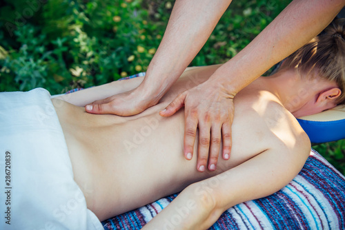 Hands masseur on the back of an unrecognizable patient close-up. Relaxed woman receives wellness massage at the Spa center outdoor.