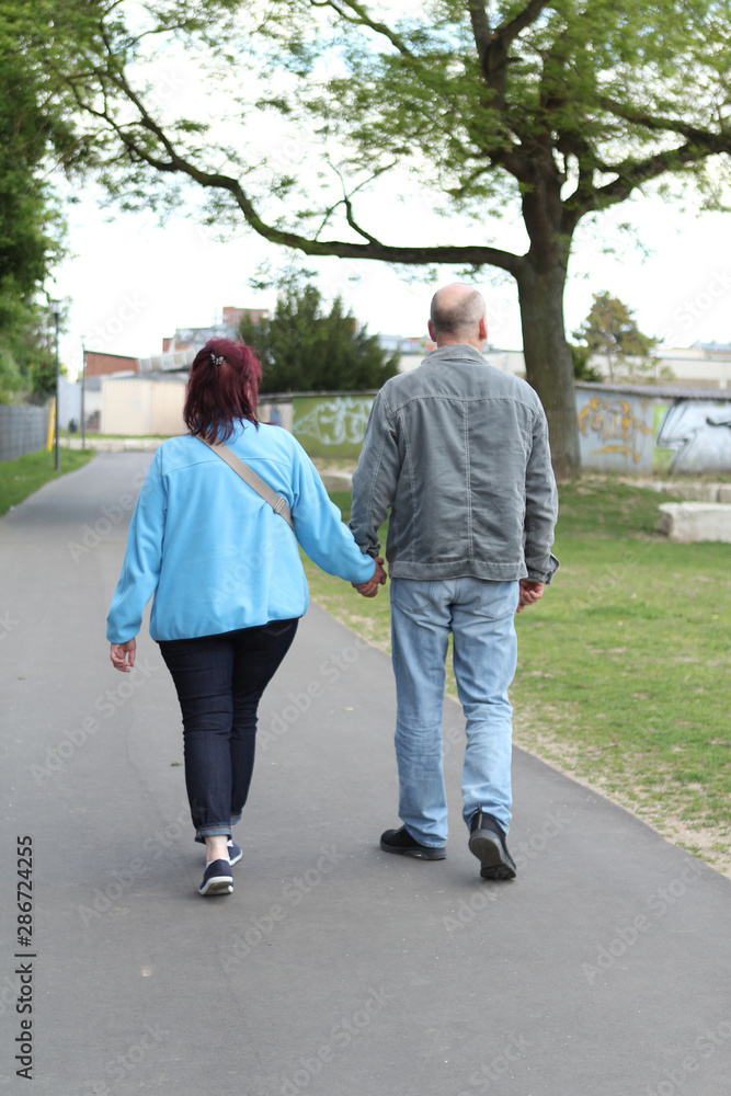 middle aged couple walking down the street holding hands, overweight woman, rear view
