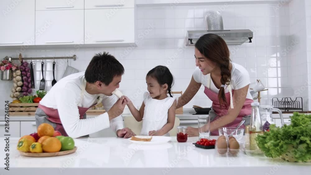 Happy Asian family make a cooking. Father, Mother and Daughter are eating breakfast in the kitchen at home. Bread with jam. Healthy food concept Happy Asian family make a cooking. Father, Mother and Daughter are eating breakfast in the kitchen at home. Bread with jam. Healthy food concept