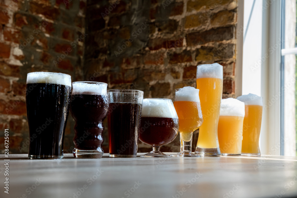 Glasses of dark and light beer and ale in sunlight on brick wall background. Cold delicious alcohol drinks are prepared for a big friend's party. Concept of holiday, fun, meeting, oktoberfest.