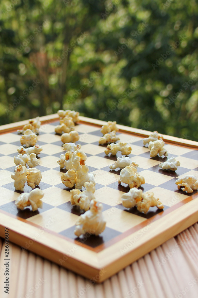 chessboard with popcorn instead of figures on a background of green summer garden, fast food concept