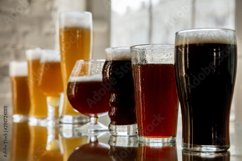 Glasses of dark and light beer and ale in sunlight on brick wall background. Cold delicious alcohol drinks are prepared for a big friend's party. Concept of holiday, fun, meeting, oktoberfest.